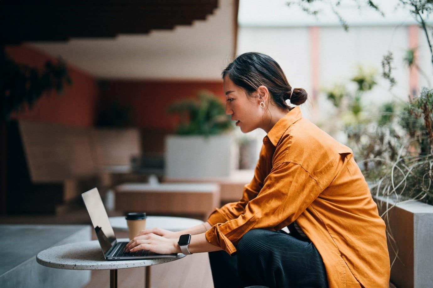A side view of someone sat in a co-working space looking at their laptop on the table