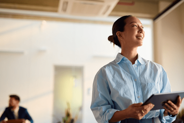 Someone stood smiling and holding an electronic tablet, they are wearing a shirt