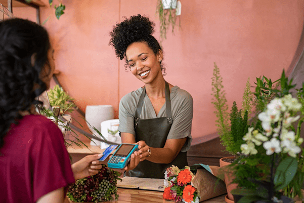A shop assistant holding a card reader, whilst a customer is tapping her card on it to pay