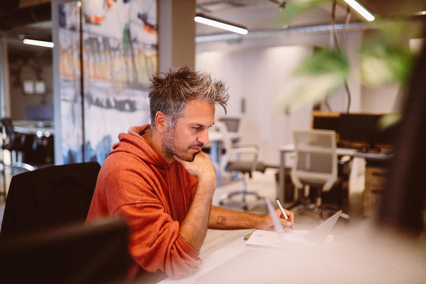 A contractor sat at a desk, making notes on a paper pad and looking at a laptop
