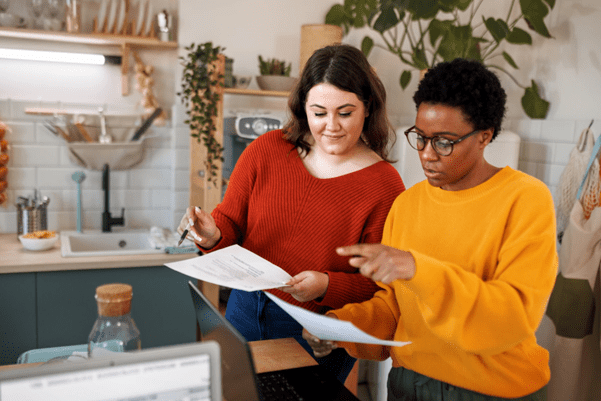 Two people sat in a kitchen looking at paperwork infront of a computer