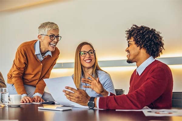 A charity trustee smiling and talking with two charity employees in a boardroom during a strategic planning meeting.