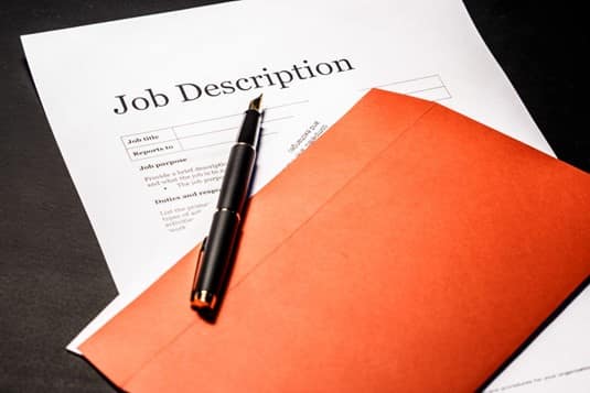 A job description laid out on a desk with an orange folder on top of it
