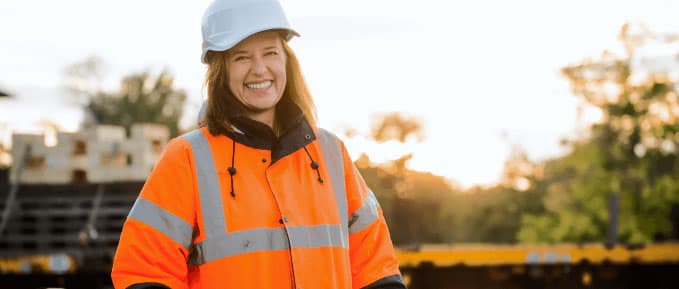 Self-employed female construction worker smiling in high-visibility jacket and hard hat on a job site.