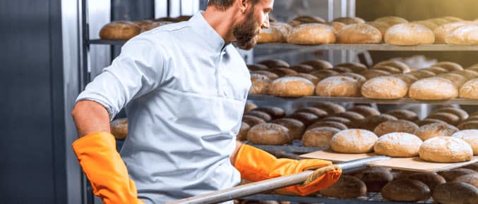 Self-employed baker removing freshly baked bread from the oven in a bakery.