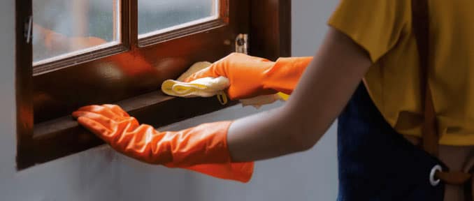 Self-employed cleaner wearing gloves while cleaning a window frame.