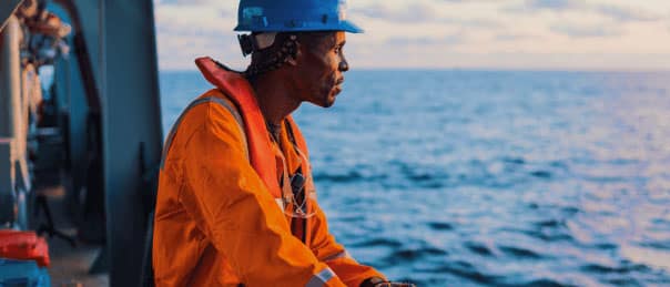 Self-employed offshore worker in protective gear looking out at the ocean from a ship.