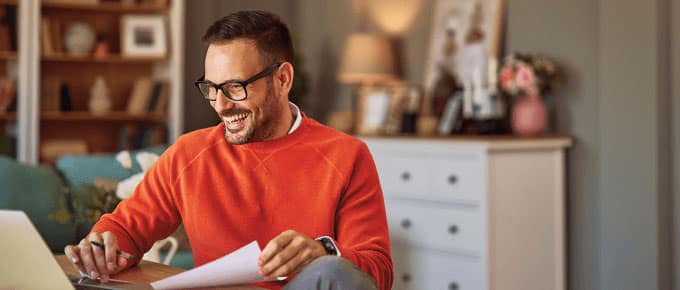 Self-employed professional happily working from home with laptop and documents.