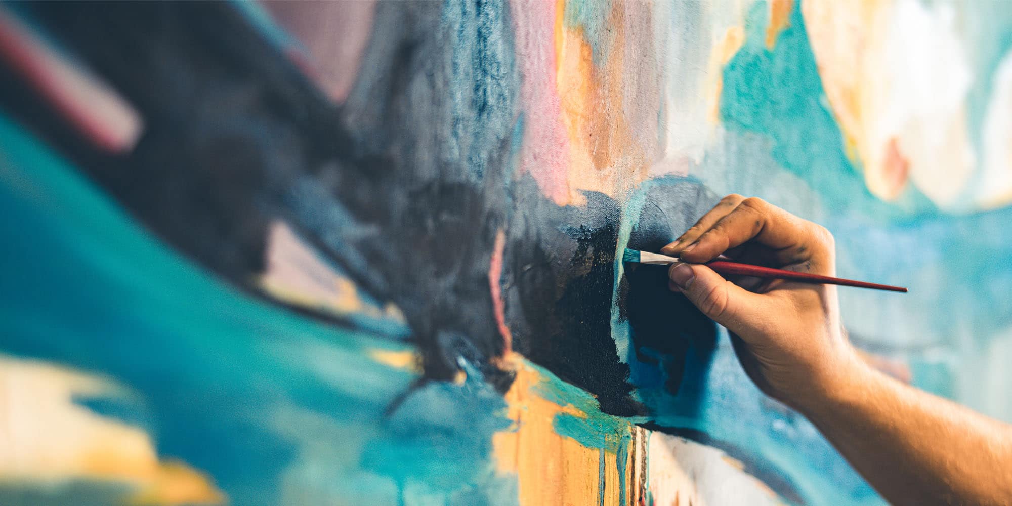 Close-up of a hand using a paintbrush to apply blue paint to a large abstract canvas