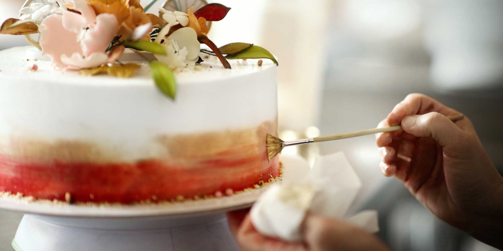 Hand using a small brush to apply color to a decorated cake