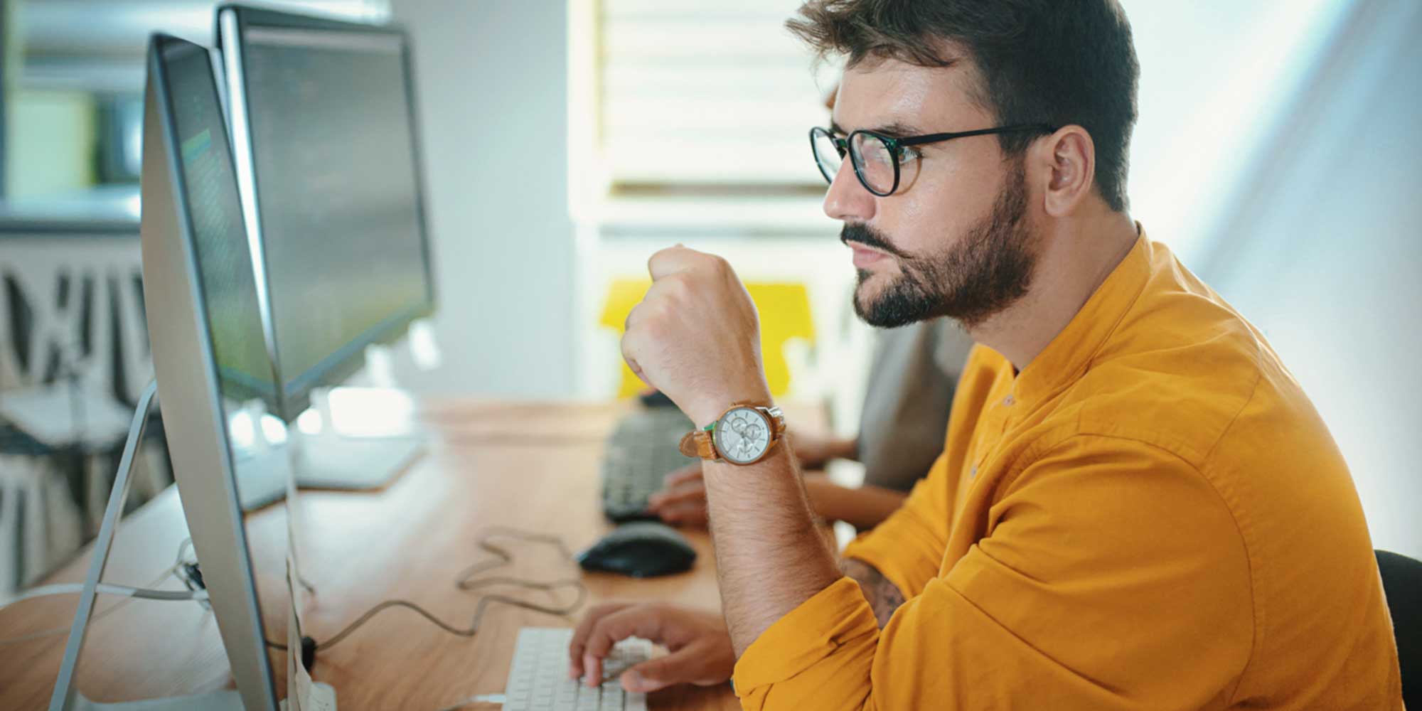 Man seated at a desk working on a computer with a large monitor