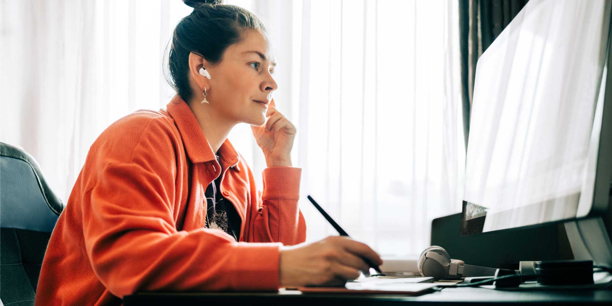 Designer working at a desk, using a stylus and tablet in front of a large computer screen