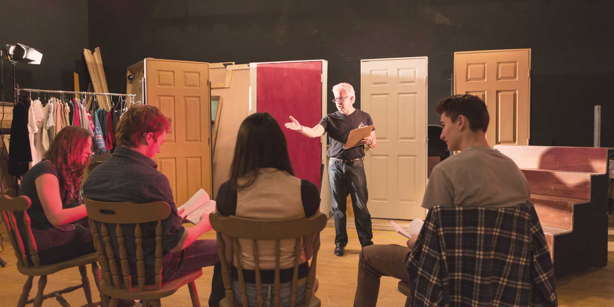 Drama teacher leading a rehearsal with students seated in a studio