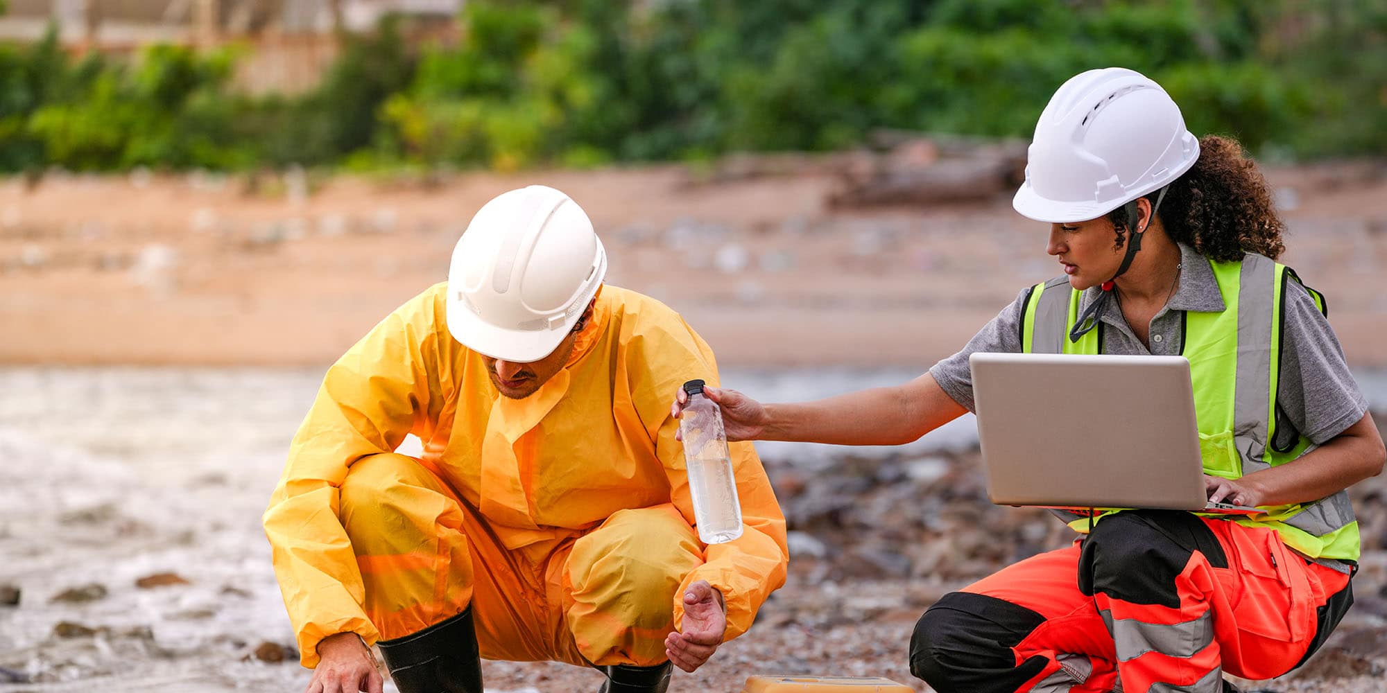 Two people conducting on‑site water sampling and data review near a body of water