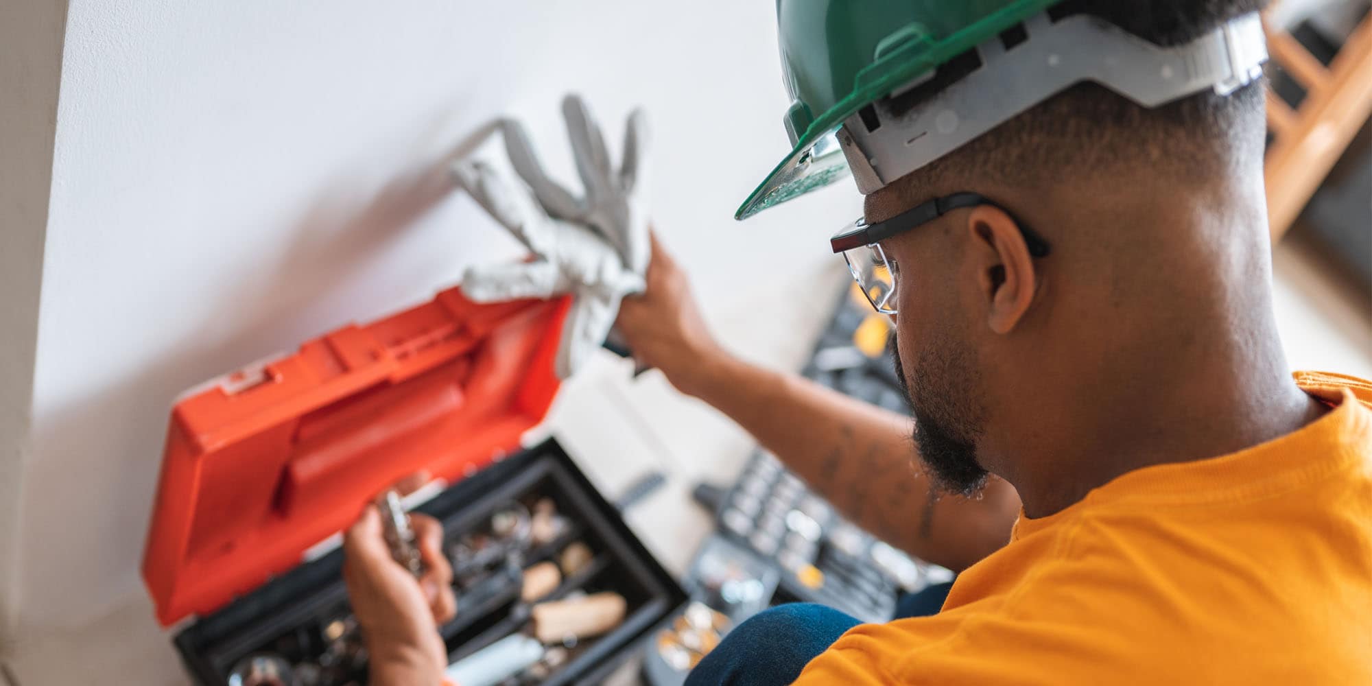 Person wearing safety glasses and a hard hat selecting tools from an open toolbox