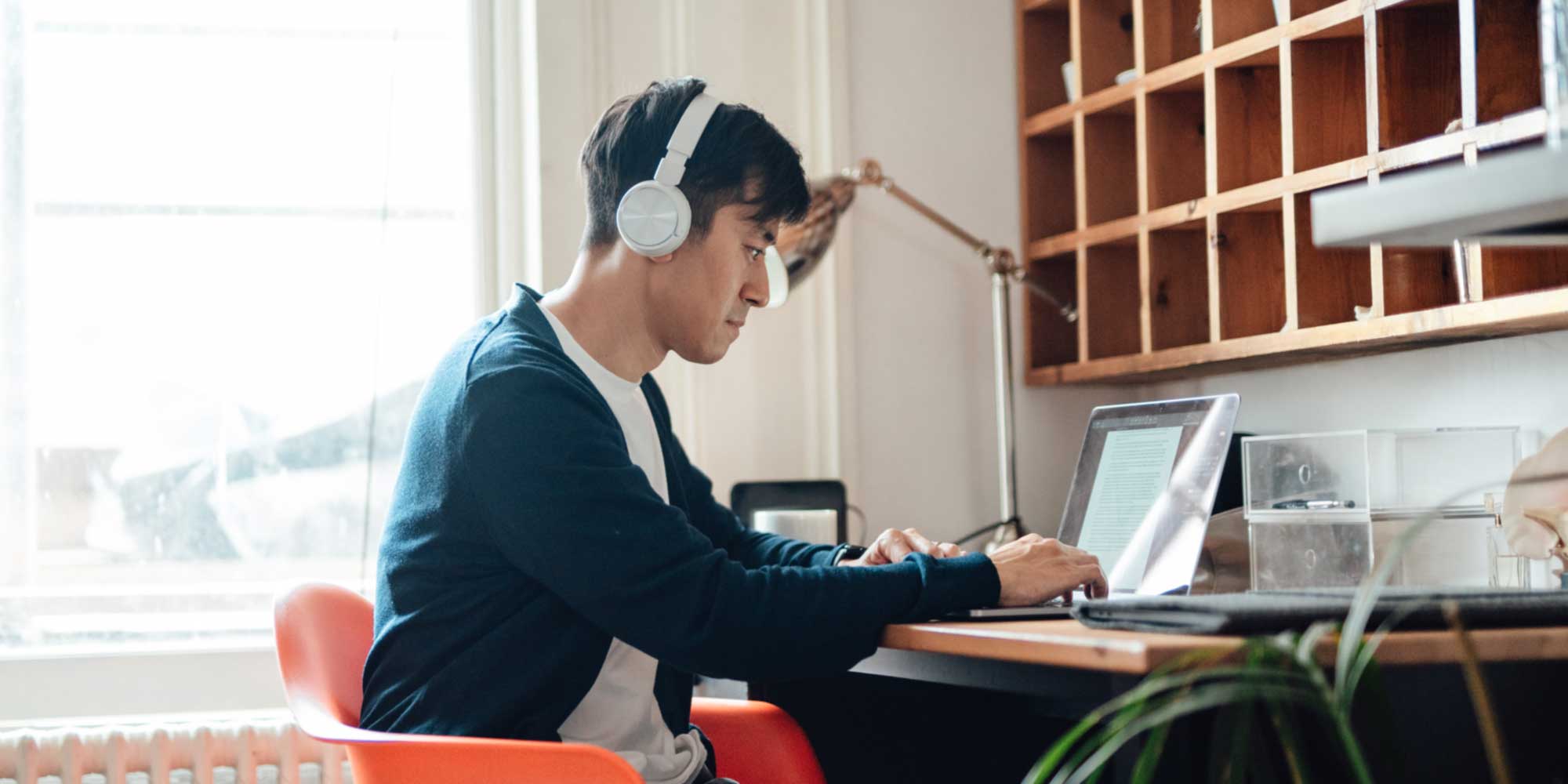 Person seated at a desk wearing headphones and typing on a laptop in a home office