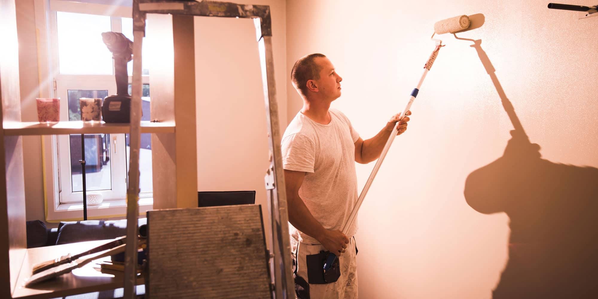 Person using a paint roller to apply paint to an interior wall