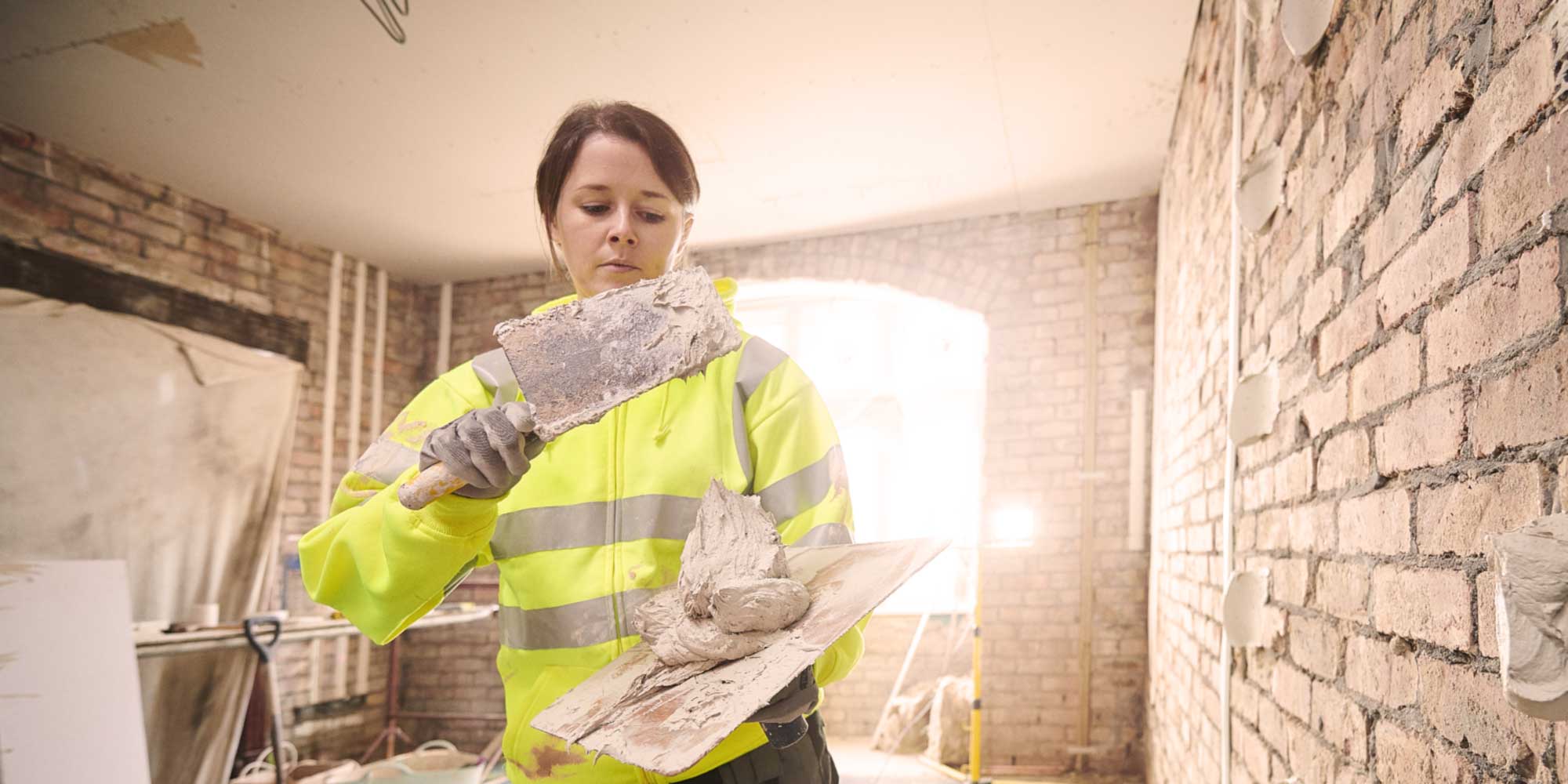 Woman applying plaster to brick wall