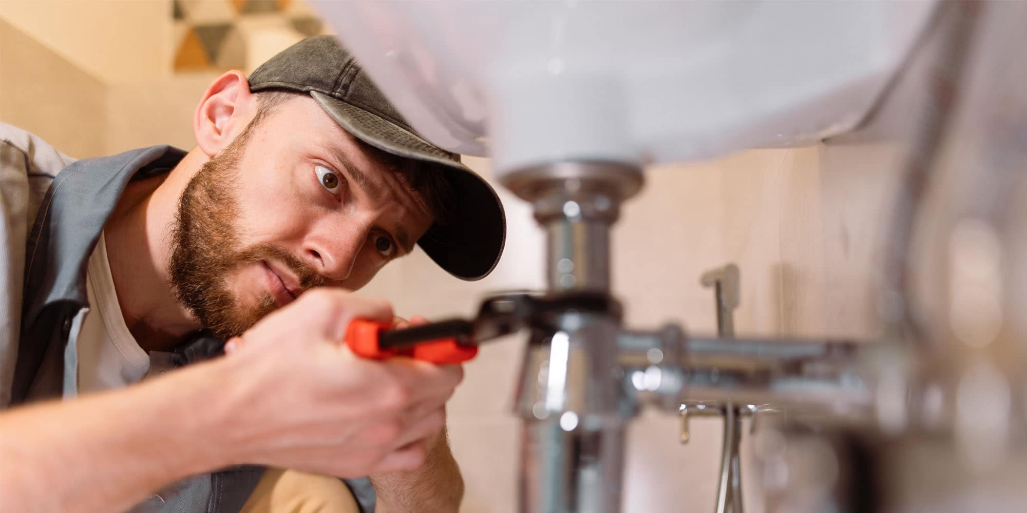 Person using a wrench to tighten plumbing connections under a sink