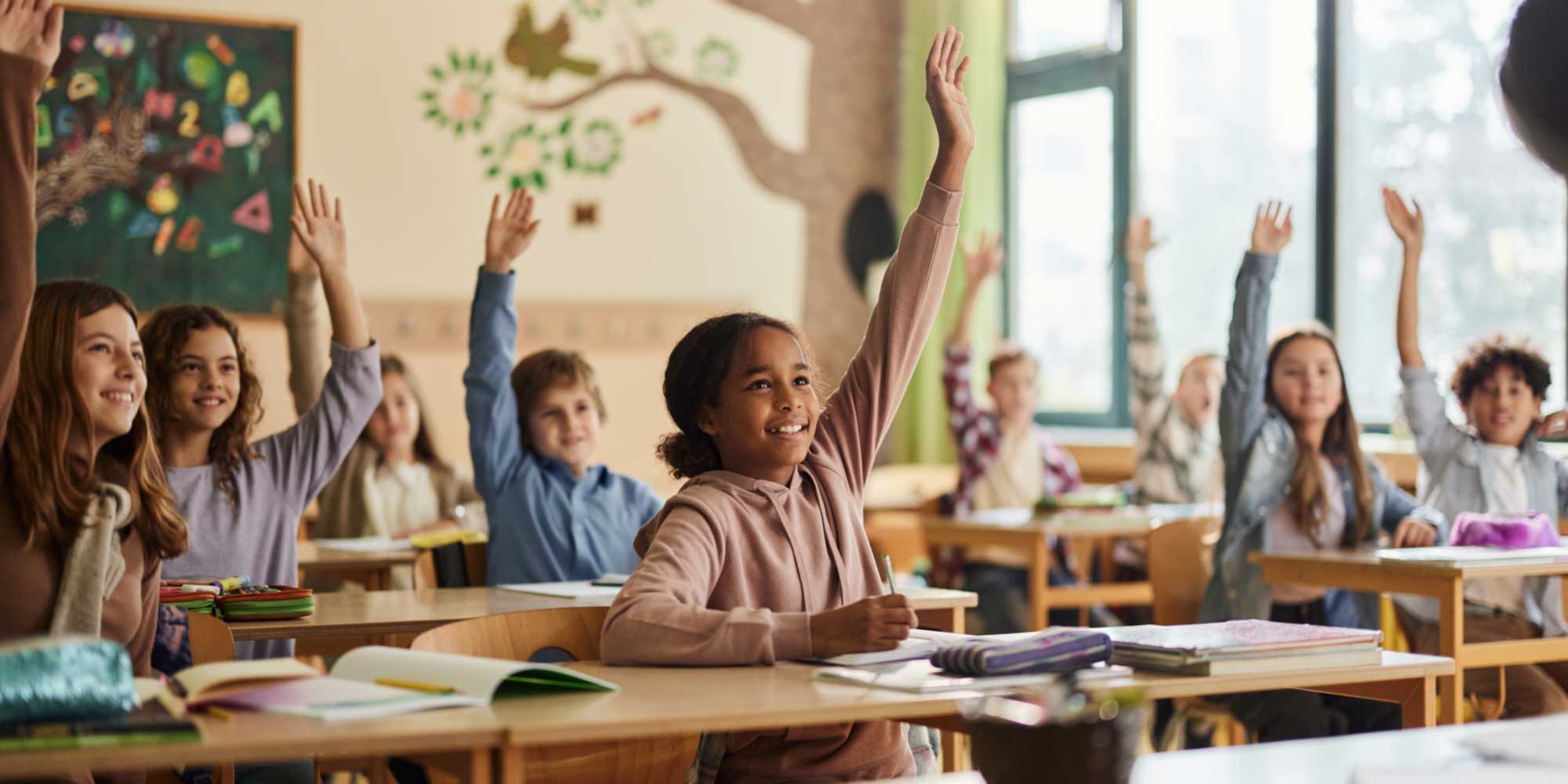 Classroom of students sitting at individual desks with hands raised