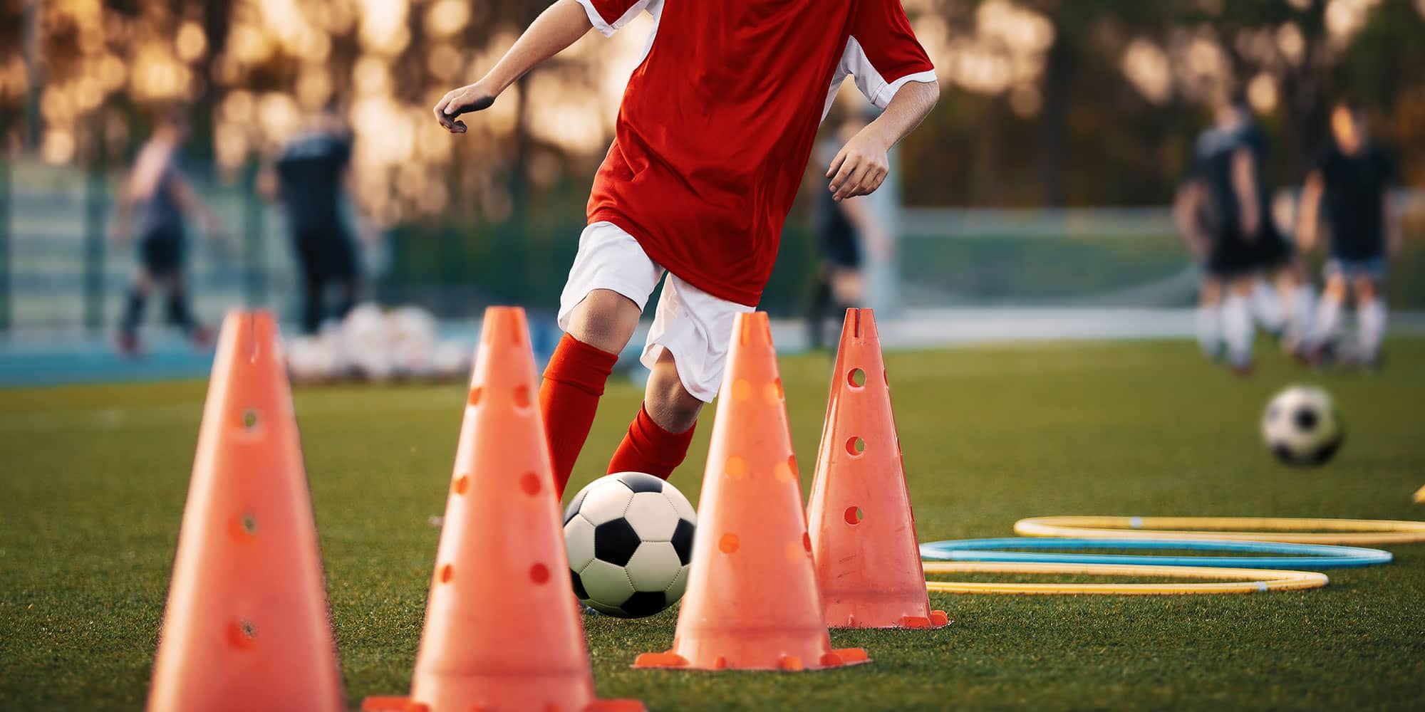 Youth football player dribbling a ball through training cones on a grassy field