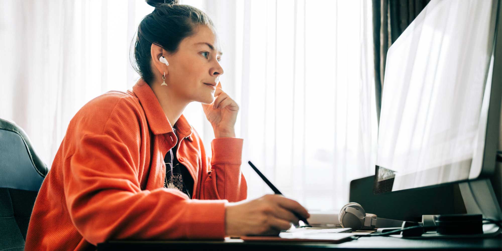 Designer working at a desk, using a stylus and tablet in front of a large computer screen