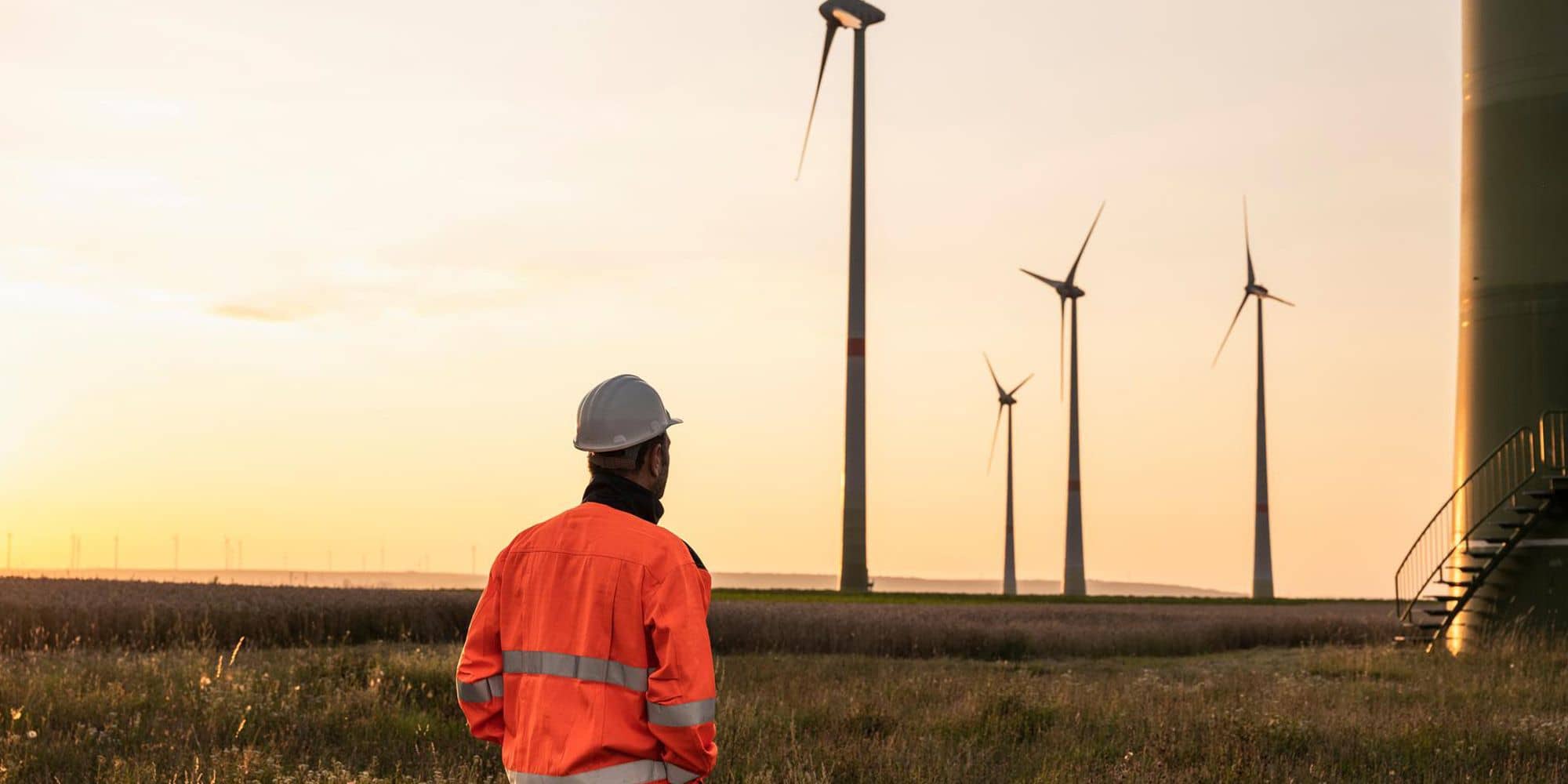 Insurance specialist surveying onshore wind farm at sunset, emphasizing risk assessment and coverage for renewable energy infrastructure.