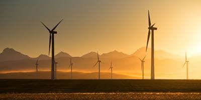 A field of wind turbines at sunset with mountains in the background, showcasing renewable energy in harmony with nature.