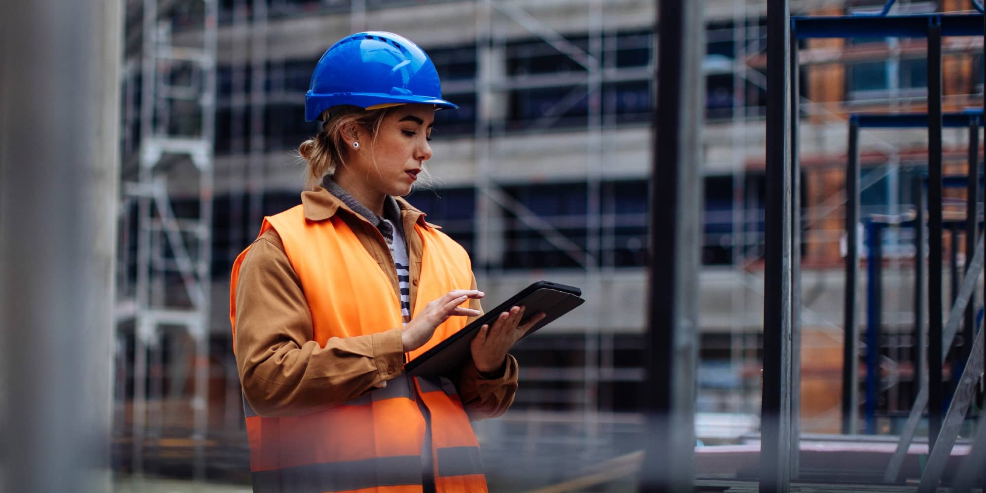 lady wearing a safety orange vest and blue hard hat typing on a tablet