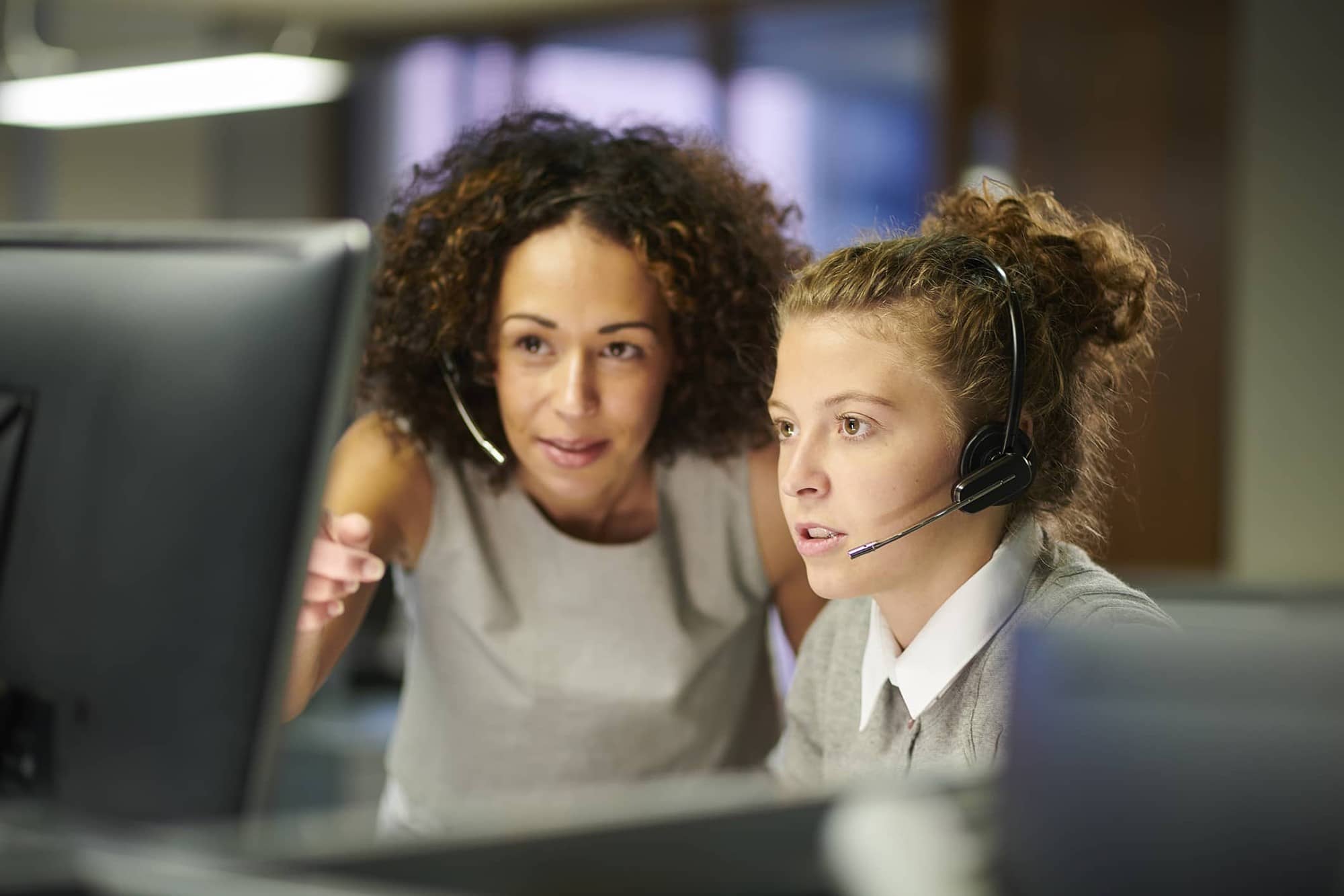 two women with headsets look at computer